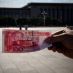 A man holding a Chinese Yuan in the middle of Tinannamen Square