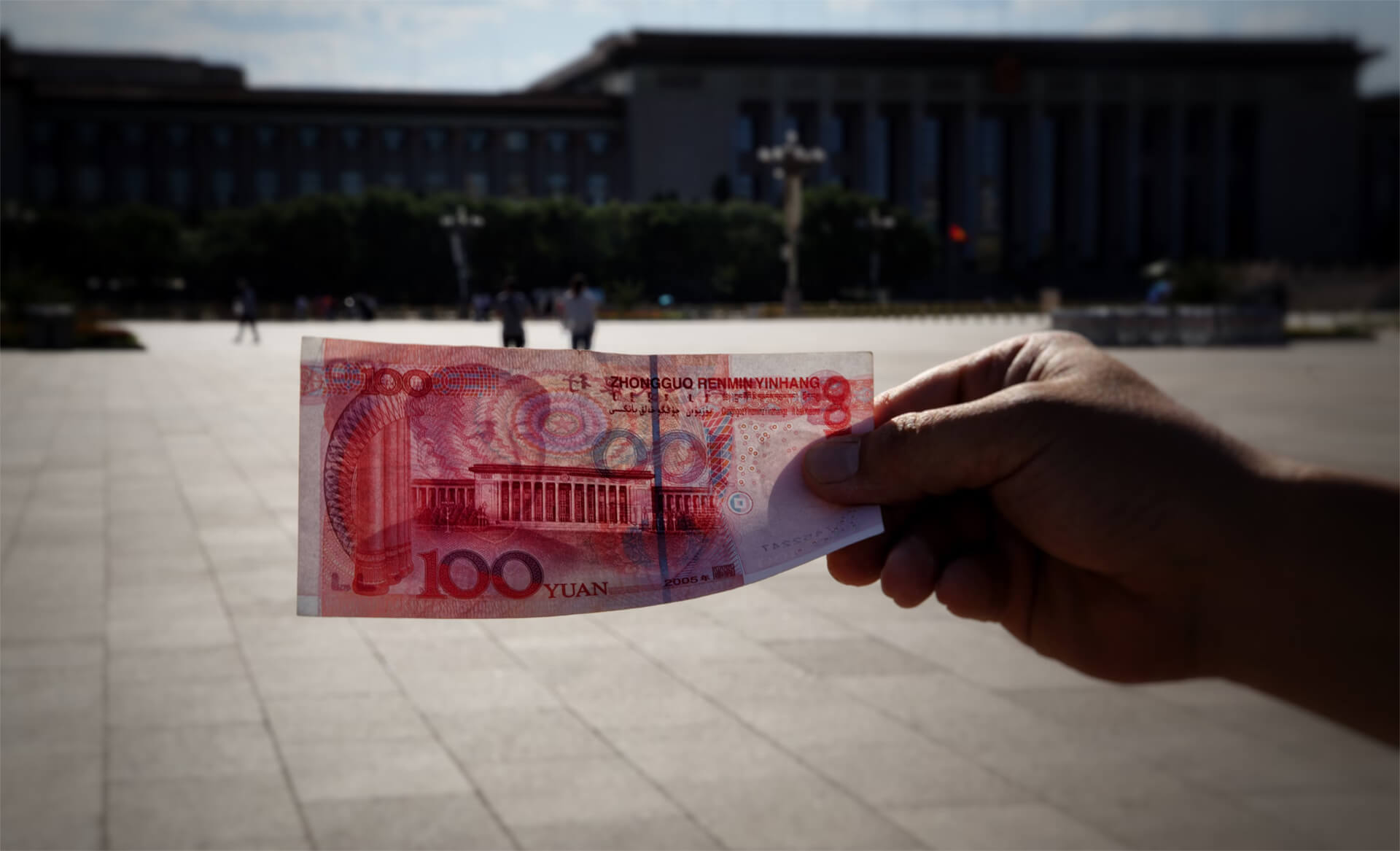 A man holding a Chinese Yuan in the middle of Tinannamen Square