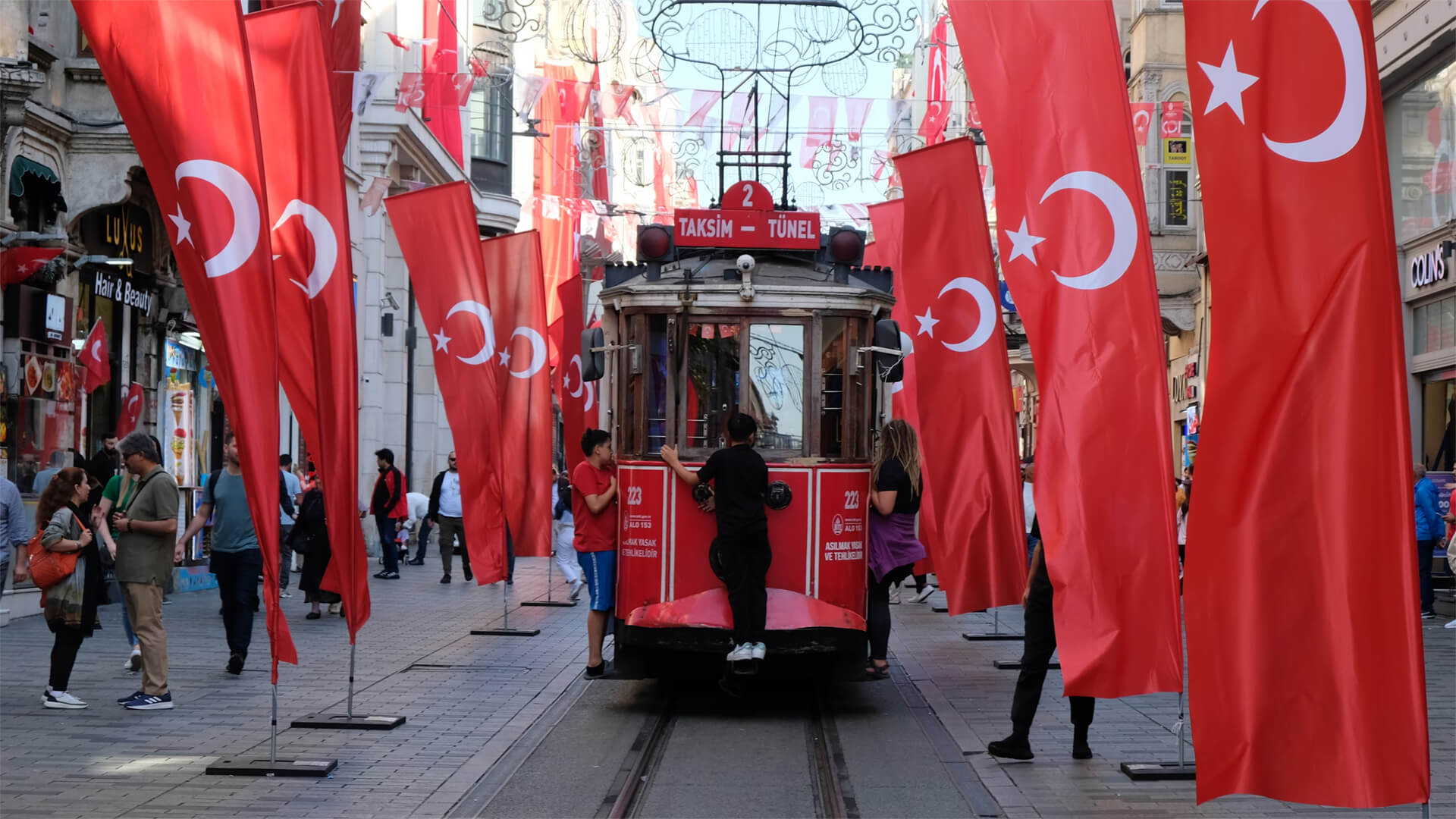 Image of a line of Turkey Flags with kids riding on the back of a tram in Istanbul