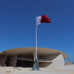 Hands holding the flag of qatar in front of a building in the middle east