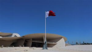 Hands holding the flag of qatar in front of a building in the middle east