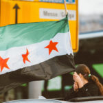 Woman holding a Syrian flag over a vehicle