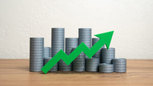 Stacks of money coins and a green arrow pointing up. Increasing income and wealth.