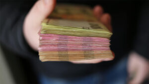 Hand offering stacks of Ukrainian money