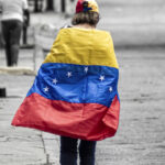 A person walking draped in a Venezuelan flag against a desaturated background