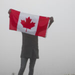 Man holding a small canadian flag against a misty background
