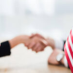 US and UK flags with a selective focus on diplomats shaking hands. Licensed by Envato Elements