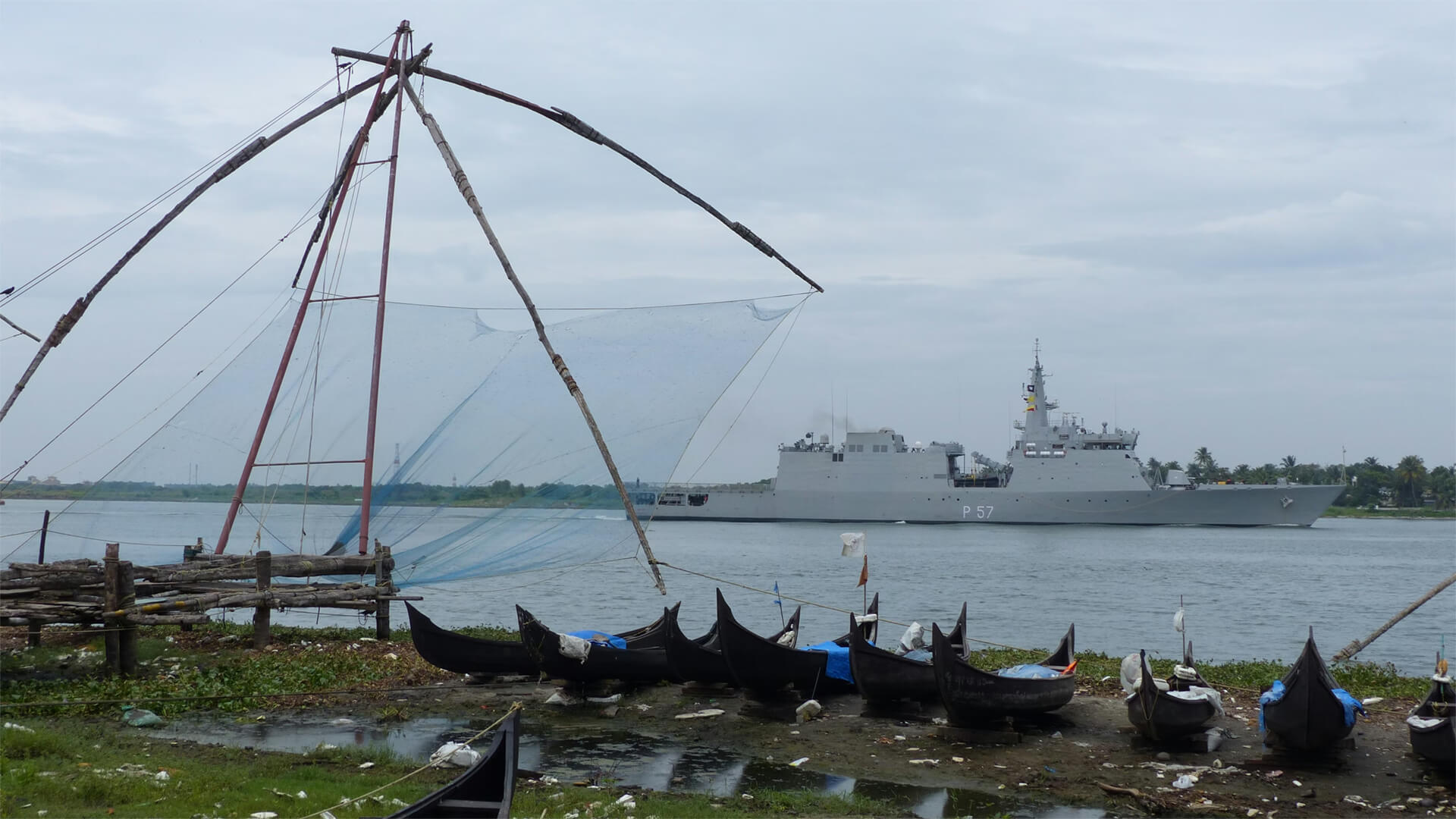 An Indian War Ship off the coast of India with fishing boats on the shore