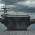 A US aircraft carrier floating in water with dark storms behind