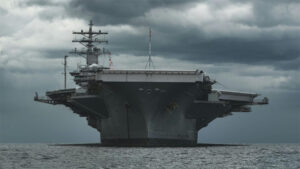 A US aircraft carrier floating in water with dark storms behind