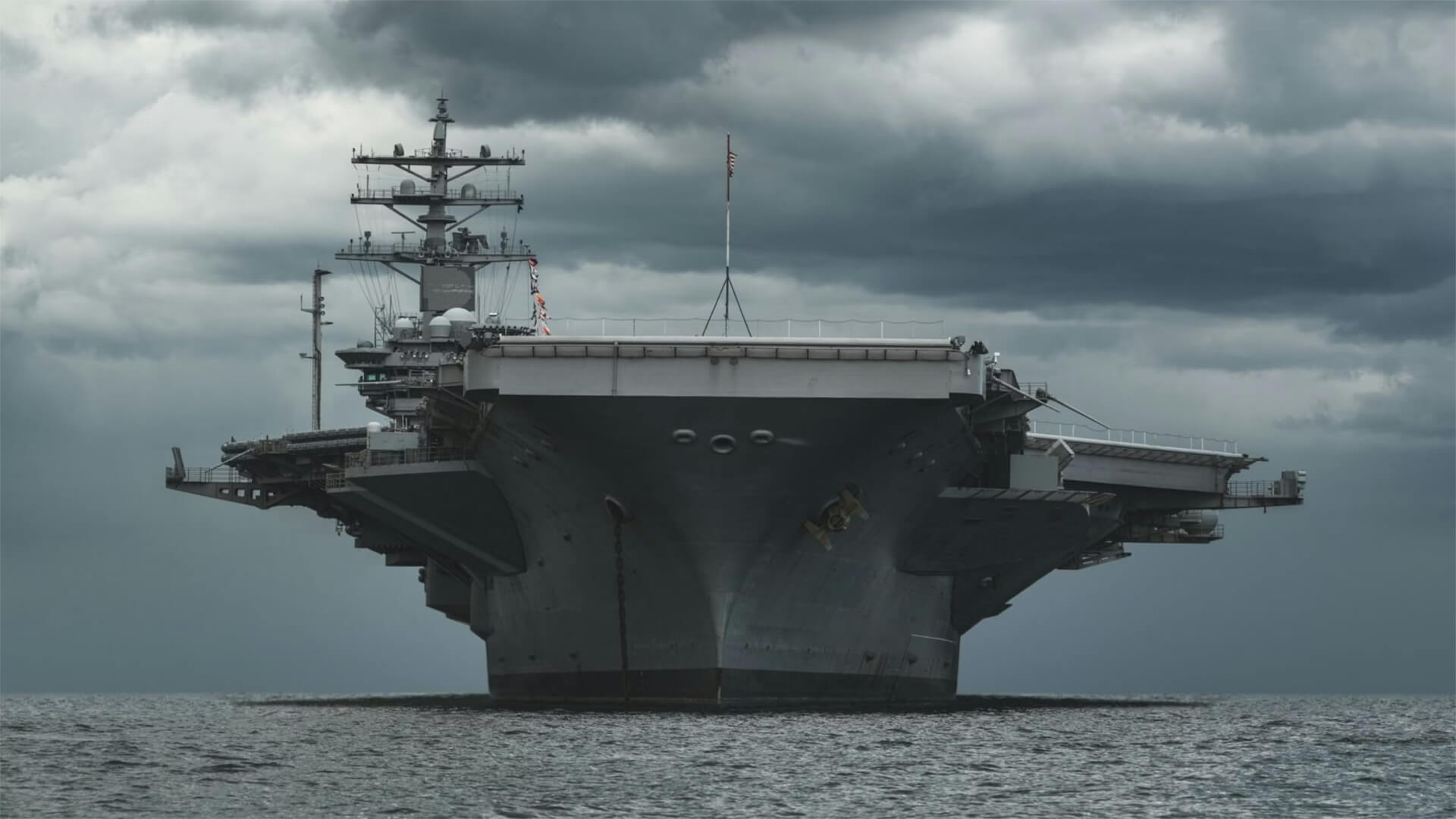 A US aircraft carrier floating in water with dark storms behind