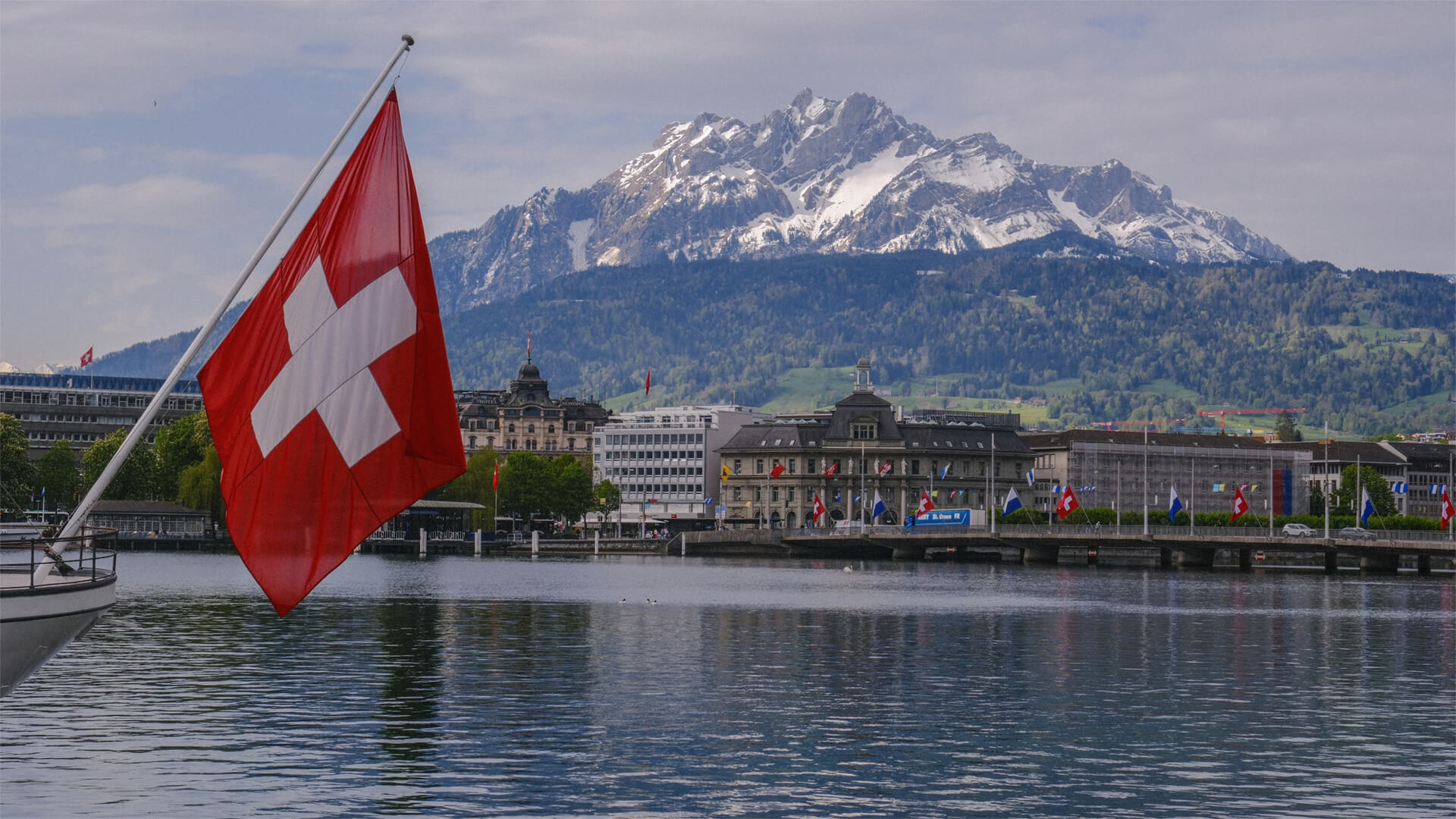 A swiss flag over the water with a city in the background