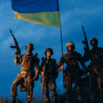 Ukrainian soldiers holding their flag against a dark sky Photo licensed by envato elements: https://app.envato.com/search/photos/1ac20b11-1fac-4c14-9452-b1e5ca99fccc?itemType=photos&term=ukraine+war