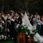 A chinese woman in a bridal dress walking down the aisle with her father and onlookers taking photos