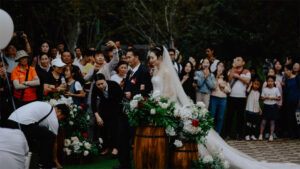 A chinese woman in a bridal dress walking down the aisle with her father and onlookers taking photos