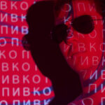 A man in sunglasses with Russian glyphs behind him on a red cyber background