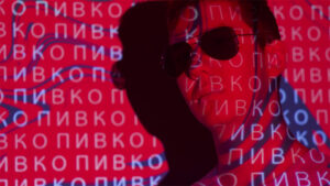 A man in sunglasses with Russian glyphs behind him on a red cyber background