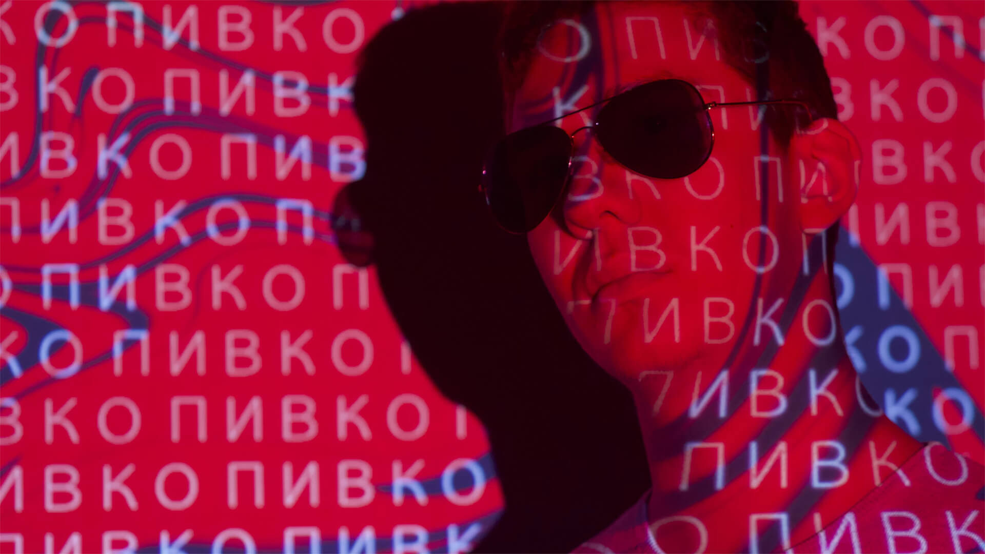 A man in sunglasses with Russian glyphs behind him on a red cyber background