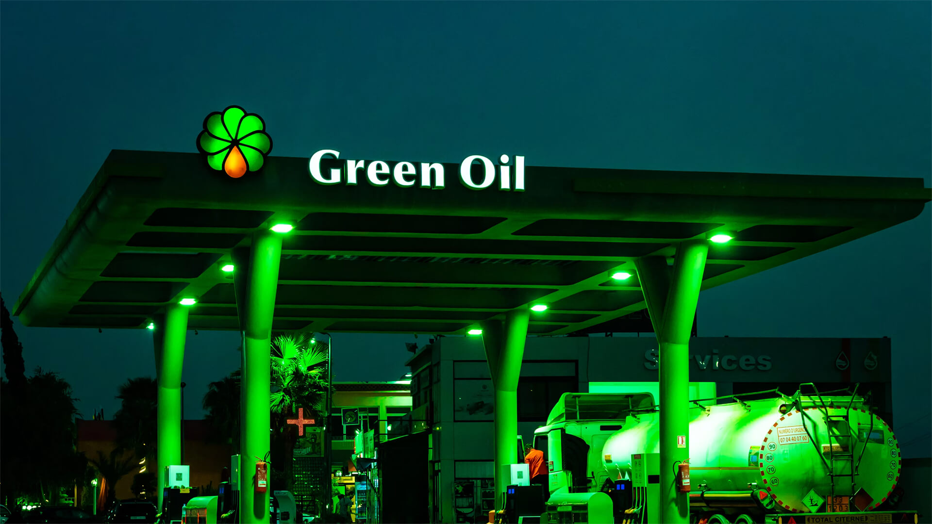 A green lit gas station with an oil tanker