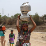 A woman and her children in India with water jugs on their head and walking