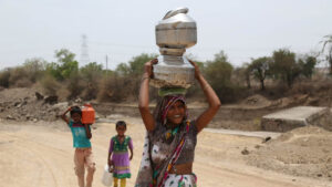 A woman and her children in India with water jugs on their head and walking