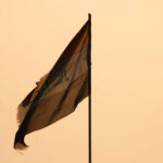Flag of Iraq, torn and tattered against a desert sun